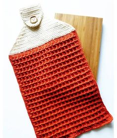 an orange and white crocheted dishcloth next to a cutting board with a wooden handle