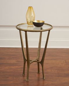 a glass table with a gold vase on top and a black bowl sitting on it