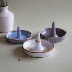 three ceramic bowls and a vase with flowers in them on a beige tableclothed surface