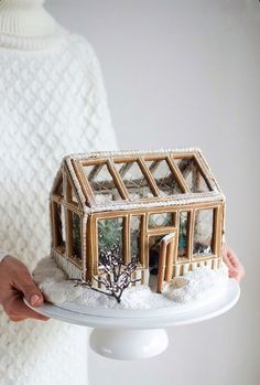 a person holding a small doll house made out of wood and fake snow covered windows