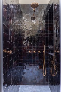 a walk in shower sitting next to a tiled wall and floor covered in black tiles