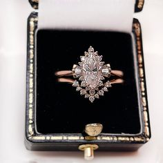 an antique diamond ring sits in a black box with gold trimmings on it