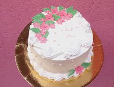 a cake with white frosting and pink flowers on it sitting on a gold plate