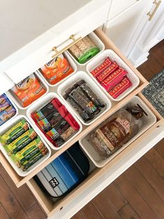 an organized kitchen drawer filled with food and drink cans on top of a wooden floor