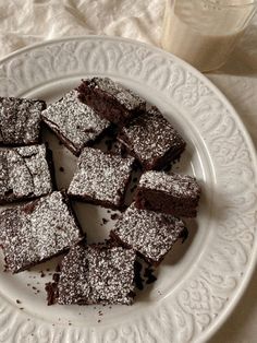 a white plate topped with brownies covered in powdered sugar next to a glass of milk