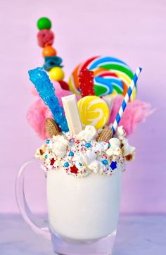 a cup filled with candy and marshmallows on top of a table next to a pink wall