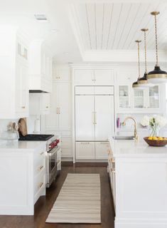 a kitchen with white cabinets and wood flooring is pictured in this image, there are two pendant lights hanging from the ceiling