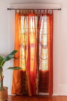 a potted plant sitting next to a window covered in orange curtains and drapes