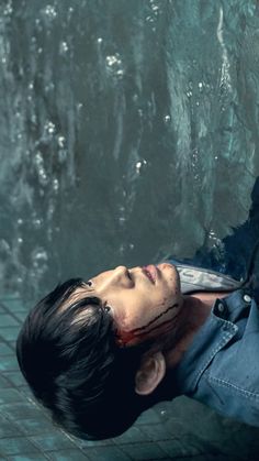 a young man with blood on his face laying down next to a water fountain and looking up at the camera