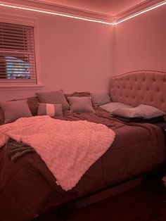 a bed with pillows and blankets on it in a room that is lit up by pink lighting