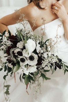 a woman in a white wedding dress holding a bridal bouquet with greenery and flowers