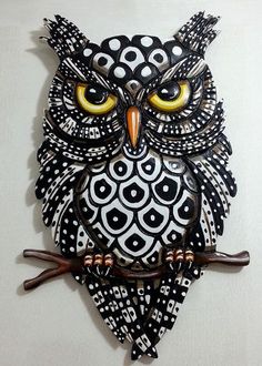 an owl with yellow eyes sitting on top of a tree branch next to a white wall