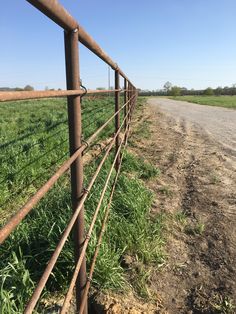 a metal fence is next to a dirt road in the middle of an open field