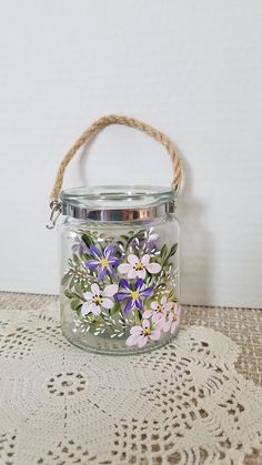 a glass jar with flowers painted on the side and rope hanging from it's lid