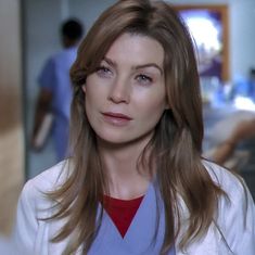 a woman with long brown hair wearing a white lab coat and red shirt looking at the camera