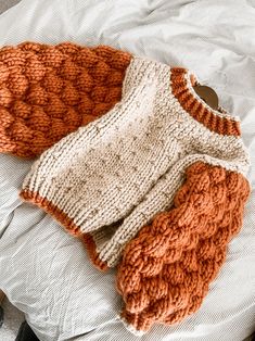 two knitted sweaters laying on top of a bed