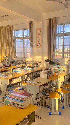 an empty classroom with many desks and books on the tables in front of large windows