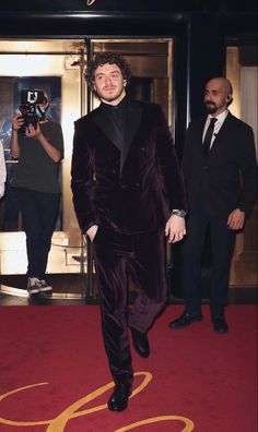 a man in a velvet suit is walking down the red carpet