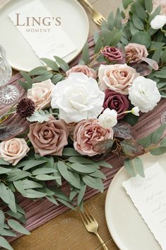 the table is set with pink and white flowers, greenery, and silverware