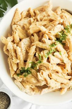 a white bowl filled with pasta and garnished with parsley on the side