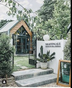 a sign that is in front of a building with plants on the steps and bushes around it