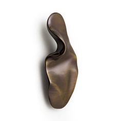 an abstract bronze sculpture is hanging on the side of a white wall and it's curved