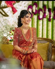 a woman sitting on top of a couch wearing a red and gold sari dress