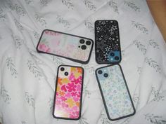 four cell phones sitting on top of a white bed covered in floral print covers and matching cases