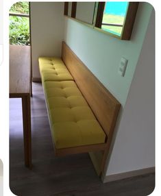 a yellow bench sitting in front of a window next to a wooden table and chair