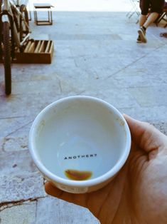 a hand holding a small white bowl in front of some benches and people sitting at tables