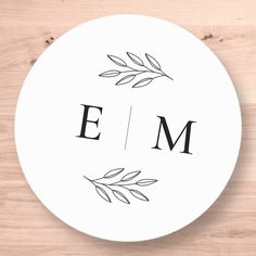 a white plate with the word em printed on it and leaves around the edges, sitting on a wooden surface