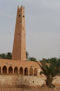 a tall tower with a clock on it's side next to a palm tree