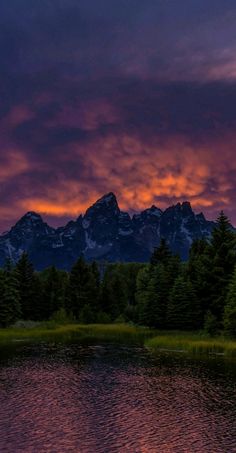 the sun is setting over a mountain range with trees and water in front of it