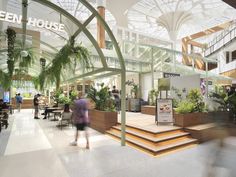 people are walking around in the lobby of an office building with plants and greenery