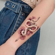 a woman with a tattoo on her arm holding a pen and snake in the shape of a flower