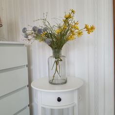 a vase filled with yellow and white flowers on top of a table next to a dresser