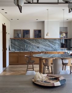 a large kitchen with marble counter tops and wooden cabinets in the center, along with two bar stools