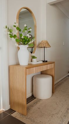 a white vase with flowers sitting on top of a wooden table next to a mirror