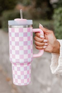 a woman holding a pink and white checkered coffee cup with a straw in it