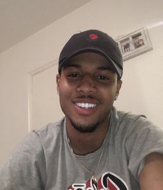 a man wearing a baseball cap smiles at the camera while sitting in front of a door