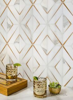 two glasses with limes on the side next to a cutting board in front of a marble tiled wall