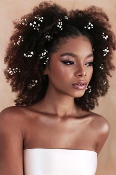 a woman with curly hair wearing a white dress and flowers in her hair, looking off to the side