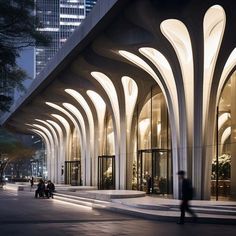 people are walking on the sidewalk in front of a building with arches and columns at night