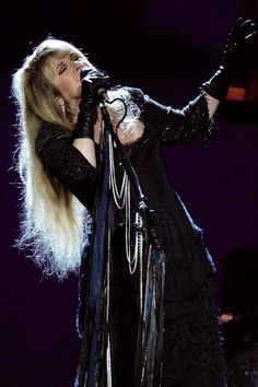 the blond haired woman is singing on stage with her hands in the air while wearing black gloves