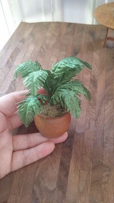 a hand holding a small potted plant on top of a wooden table