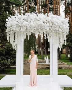 a woman standing in front of a white structure with flowers hanging from it's ceiling