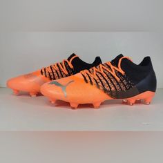 an orange and black soccer shoe with spikes on the soles, against a white background