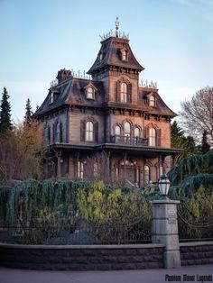 an old victorian style house with ivy growing on the front and side fence around it