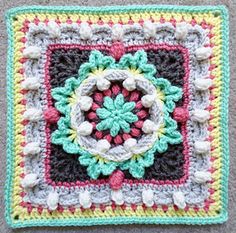 a crocheted square with a flower in the center on a gray carpeted floor