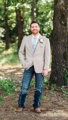 a man standing in front of a tree wearing a gray suit and blue tie with his hands in his pockets